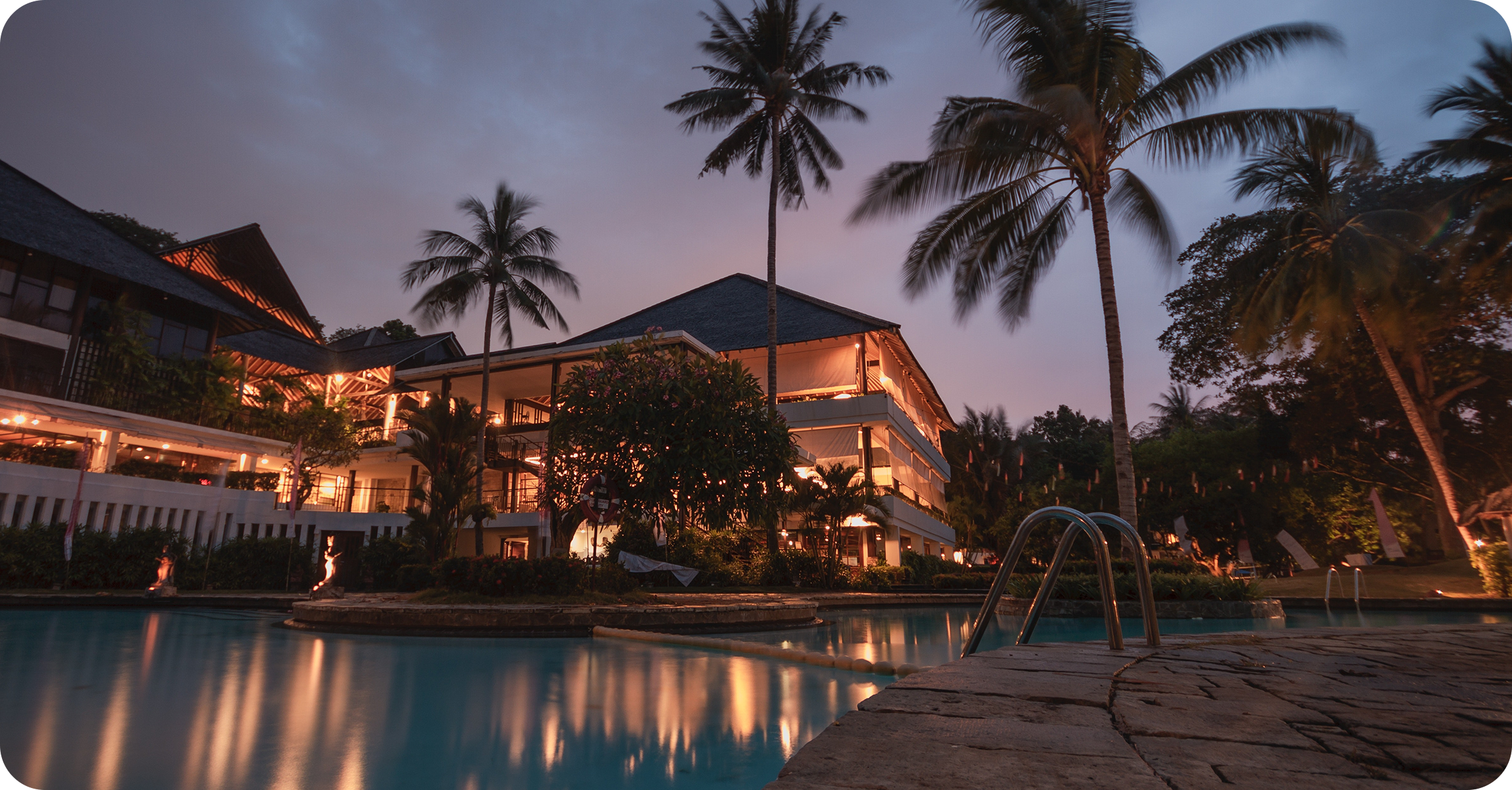 Dusk image of a softly lit luxurious hotel with a swimming pool 